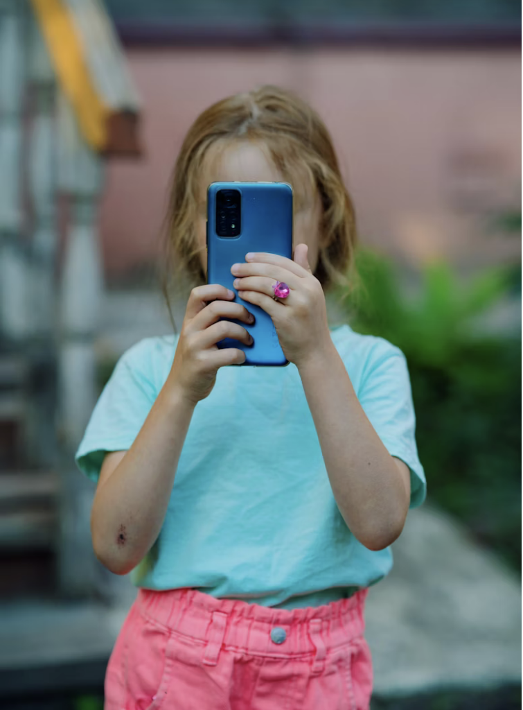 dziewczynka ze smartfonem w rękach, twarz przysłonięta smartfonem