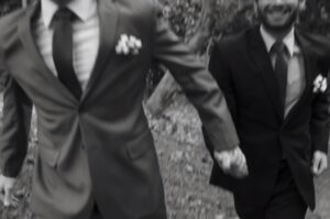 czarnobiała fotografia, 2 panów młodych biegnie trzymając się za ręce, widać tylko garnitury
