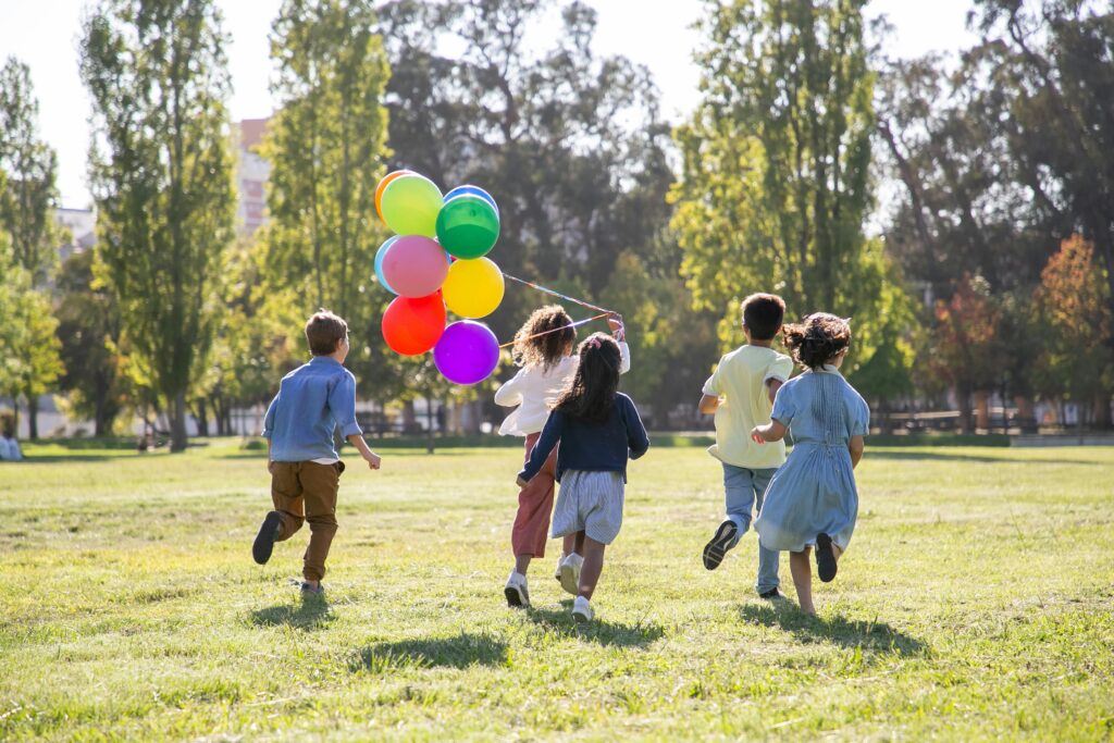 wiosna, dzieci biegną z balonikami w stronę drzew