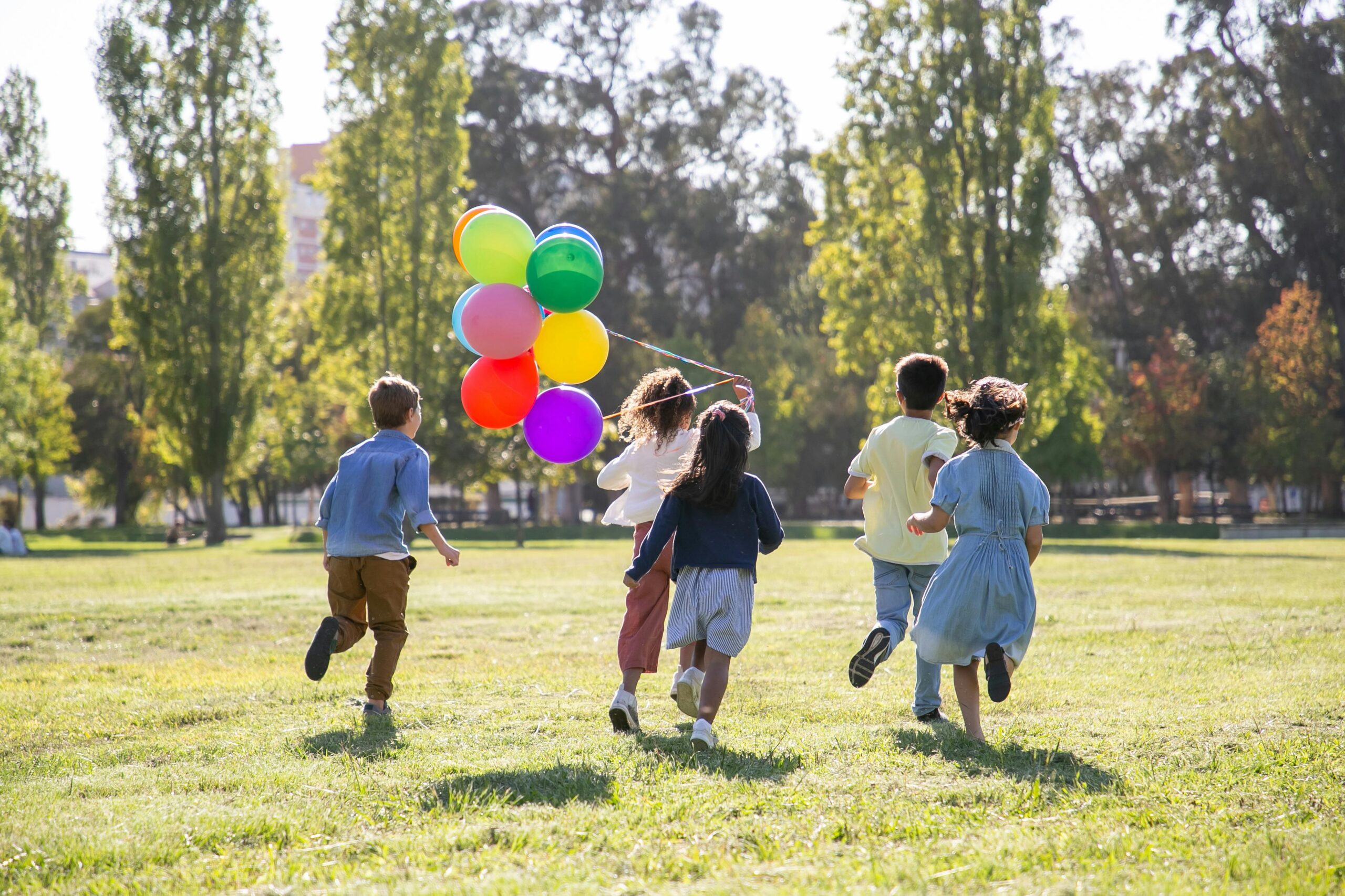 wiosna, dzieci biegną z balonikami w stronę drzew