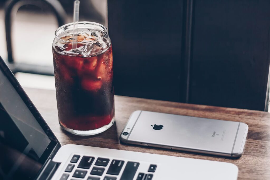 mrożona kawa z kostkami lodu lub cola, w tle laptop i smartfon
